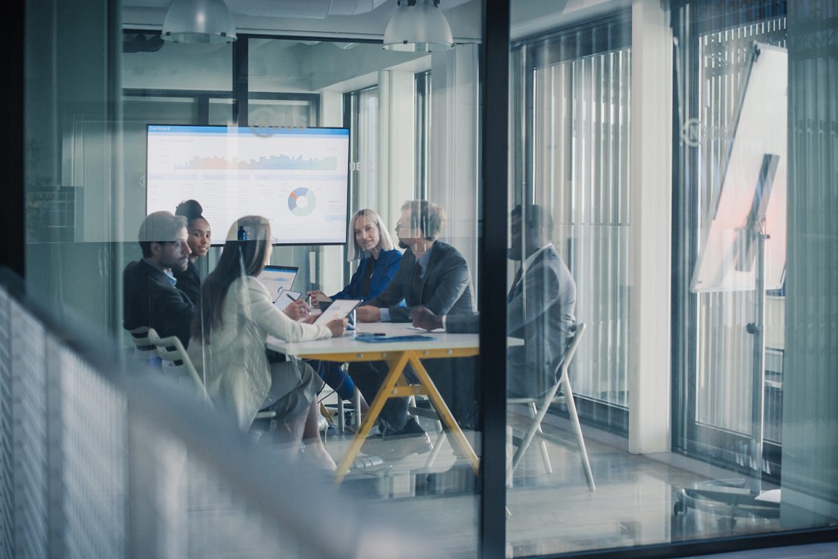 Business Team Meets in a Glass Conference Room to Review Performance Dashboards, Share Ideas, Plan Client Work, and Coordinate Digital Projects Using Laptops, Charts, and Reports on Business